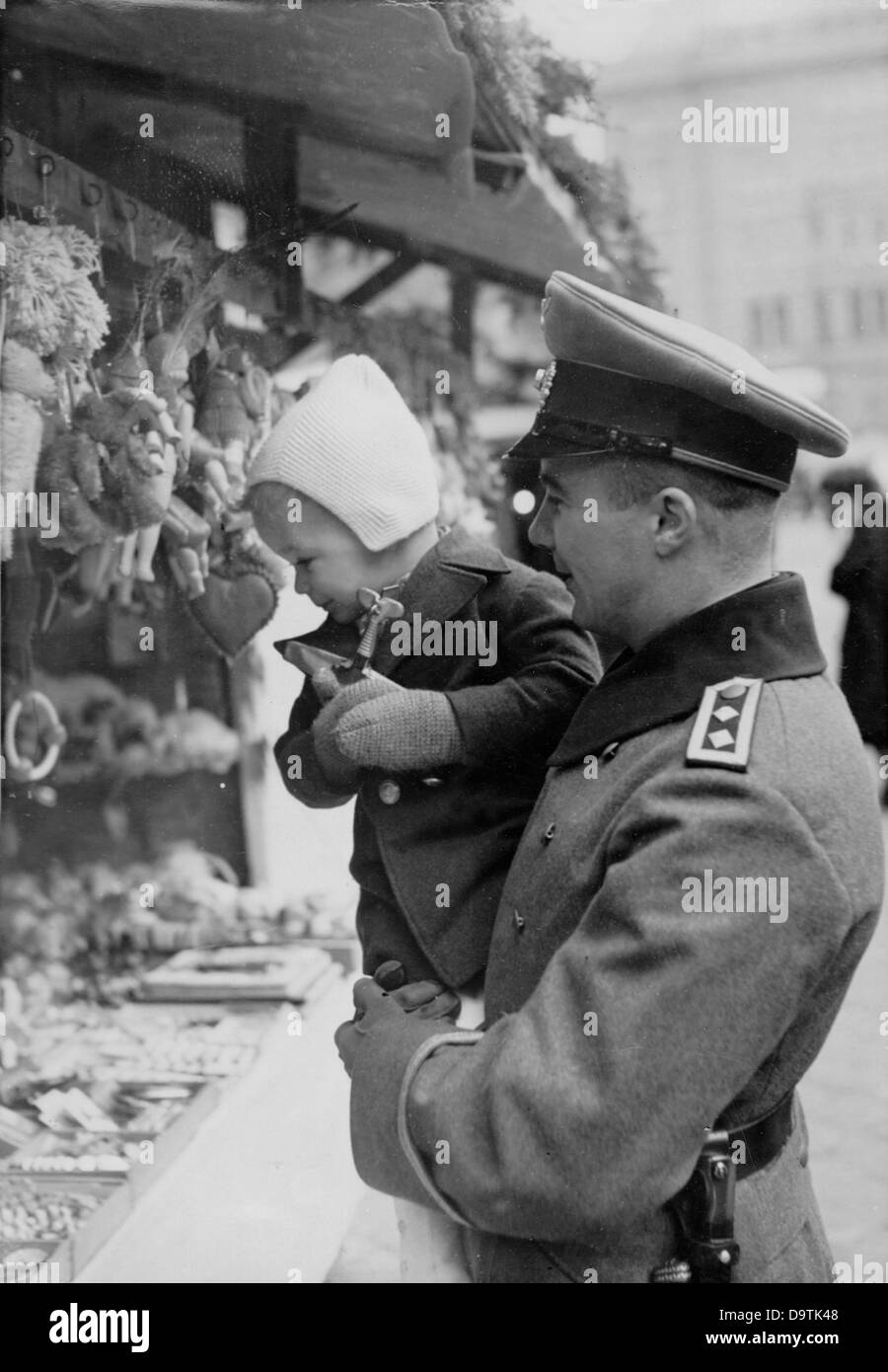 Un soldat allemand de Wehrmacht en fourrure transporte son enfant autour du marché de Noël en hiver 1940. Lieu inconnu. Fotoarchiv für Zeitgeschichte Banque D'Images