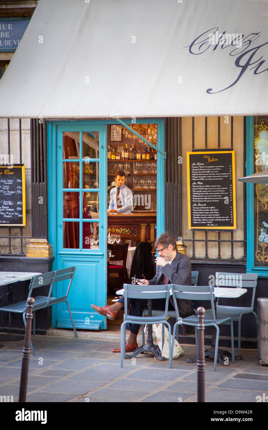 Homme assis près de la porte de chez Julien - un café dans l'Arrondissemont Paris 4ème, France Banque D'Images