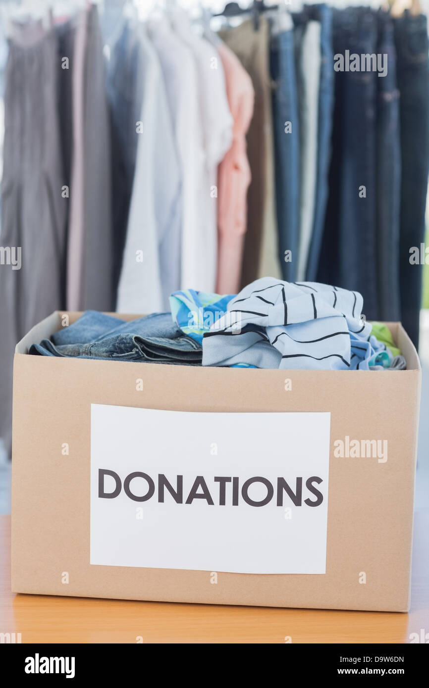 Boîte de dons rempli de vêtements en face de tringle Banque D'Images
