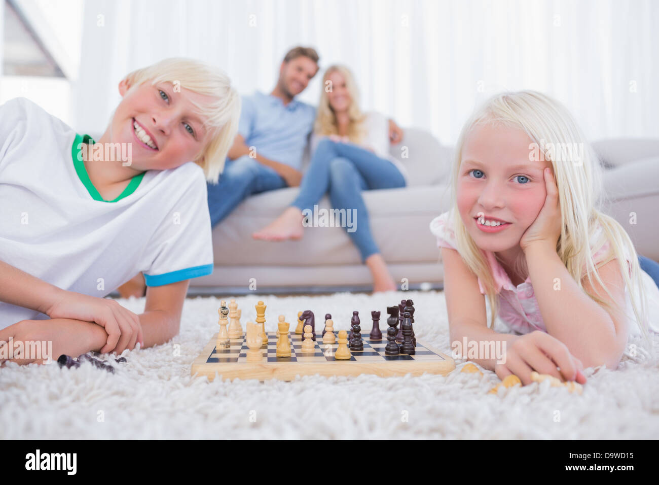 Enfants jouant aux échecs en face de leurs parents Banque D'Images