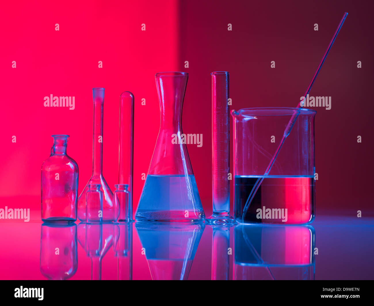 Fond rouge avec des contenants en verre et leur réflexion sur une table dans une lumière bleue Banque D'Images