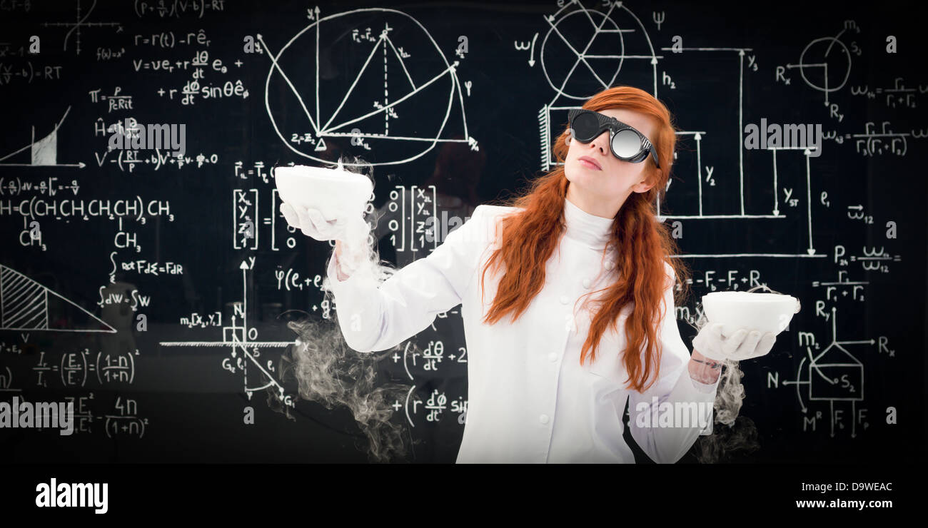 Young female scientist comparant deux pots devant un tableau rempli de formules chimiques dans le laboratoire de chimie Banque D'Images