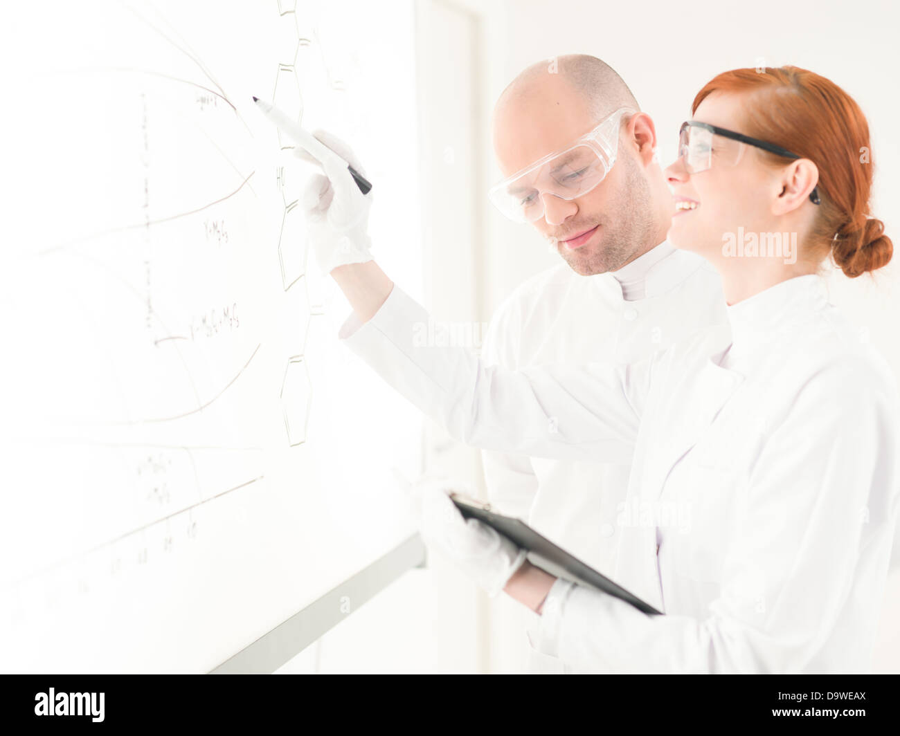 Deux scientifiques dans un laboratoire ayant une discussion et le partage des données comme la femme dessine des diagrammes sur une carte en verre ou d'une interface avec un feutre Banque D'Images