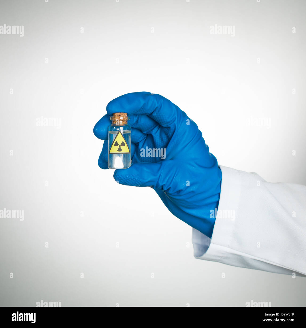 Fond blanc avec la main dans le gant et bleu sarrau blanc tenant une petite bouteille transparente appelée matières radioactives avec un liquide incolore transparent Banque D'Images