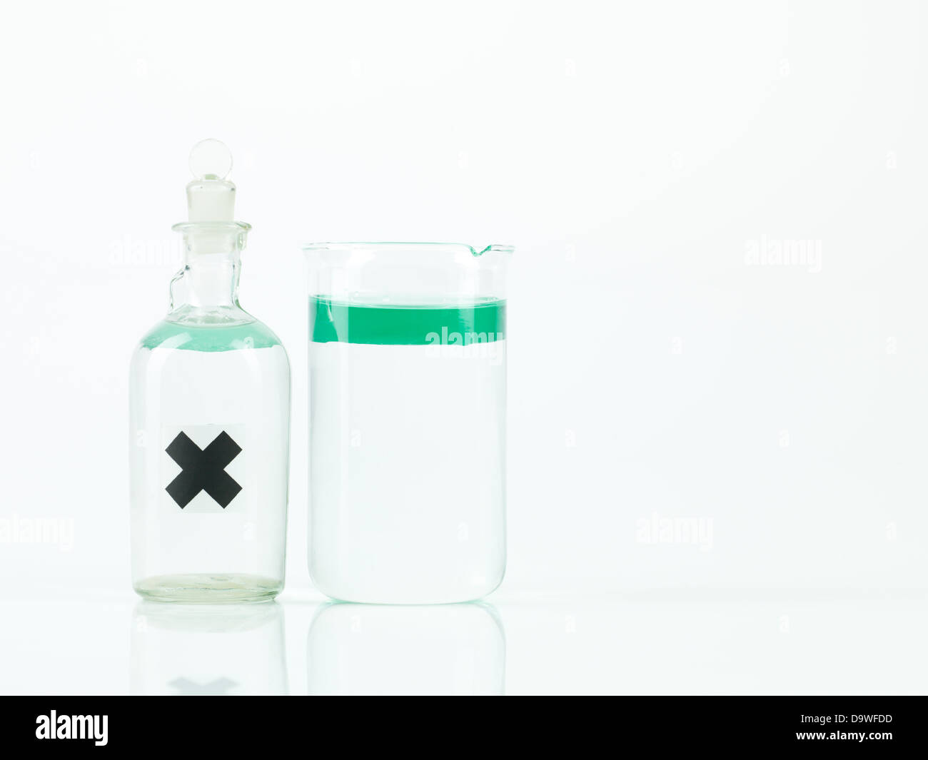 Deux récipiendaires, une bouteille en verre et une tasse, berzelius contenant un liquide vert transparent flottant au-dessus d'un liquide incolore transparent, l'une marquée d'une étiquette x noir, avec un fond blanc Banque D'Images