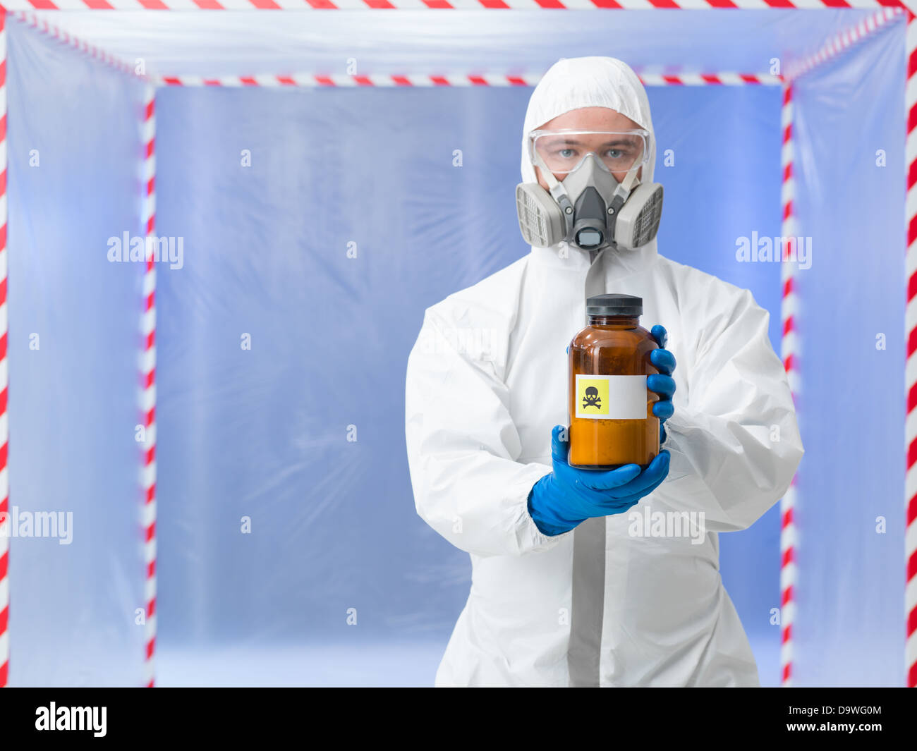 Portrait d'un homme portant un équipement de protection tenant une bouteille étiquetée comme substance mortelle, dans une chambre surounde avec bande rouge et blanc Banque D'Images