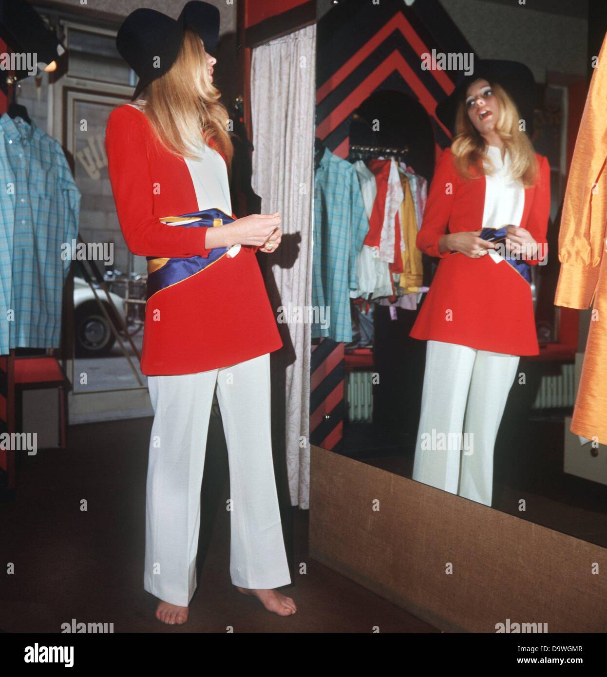 Une jeune femme a un regard dans le miroir et se demande si les vêtements offerts par une boutique à Francfort son costume. Photographié dans les années 1970. Banque D'Images