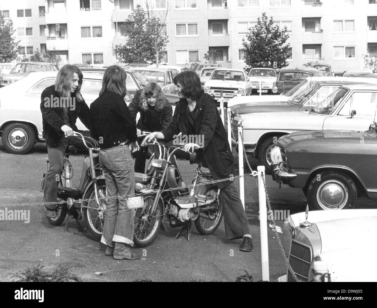 Quatre adolescents aux cheveux longs avec leur parler en cas d'un parking, photographié au début des années 70. Banque D'Images