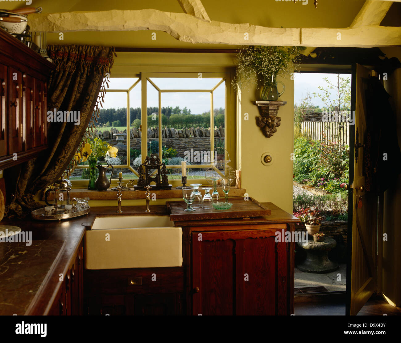 Old fashioned Belfast disparaître sous fenêtre dans country style cuisine avec porte ouverte et poutres au plafond rustique peint crème Banque D'Images
