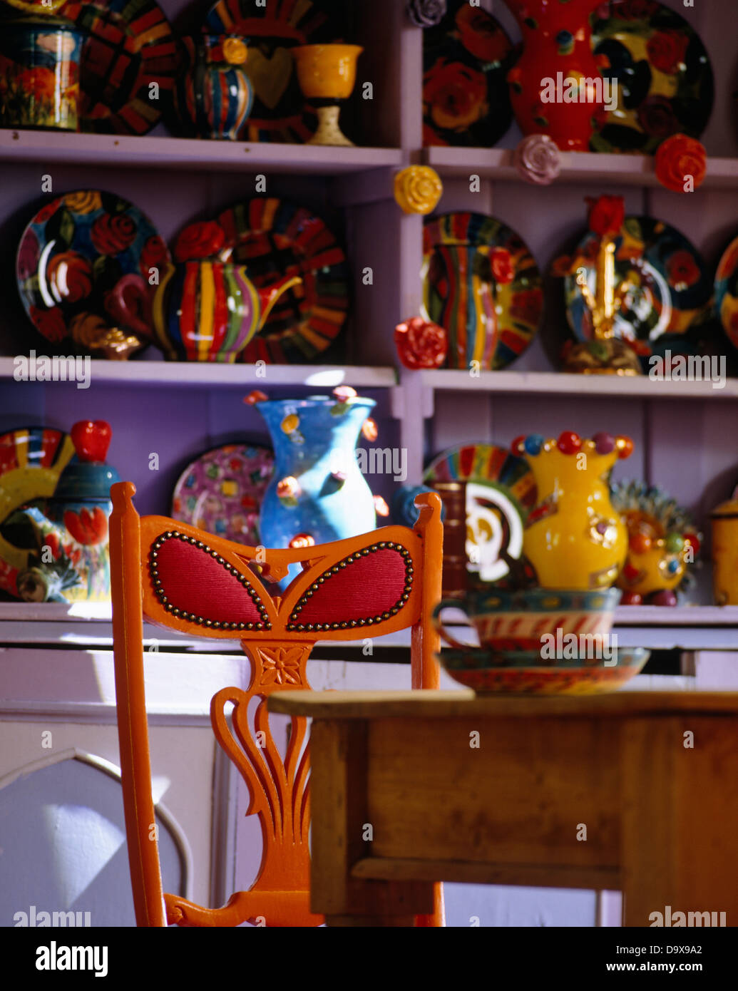 Orange à rouge +chaise simple en bois table en face de collection de poteries colorées sur étagères violet Banque D'Images