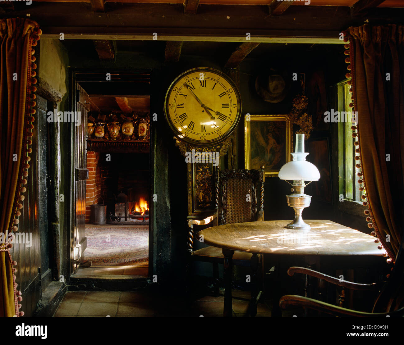 Horloge antique et de la vieille table en bois avec lampes en laiton dans la région de Tudor cottage salle à manger avec poutres apparentes au plafond bas Banque D'Images