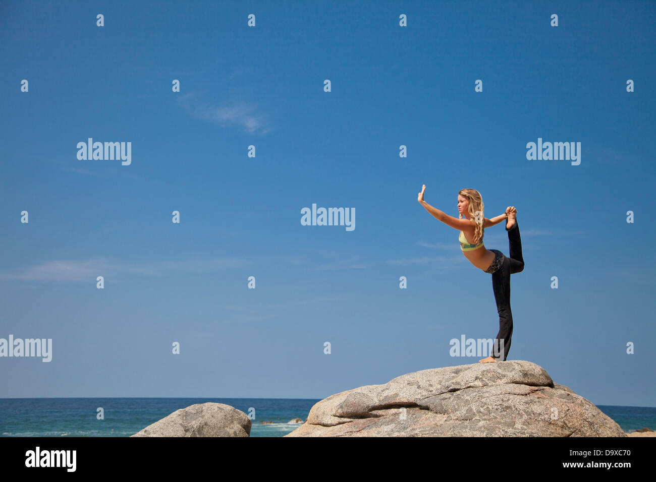 Jeune femme en yoga pose sur la roche par ocean Banque D'Images