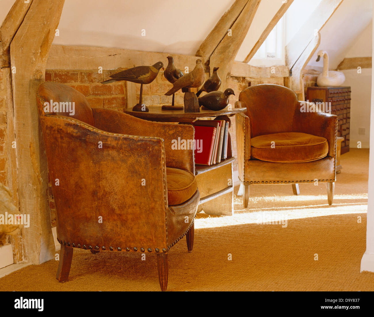 Deux fauteuils en cuir et table en chêne avec collection de leurres pigeon sculpté et peint dans cette chambre mansardée Banque D'Images