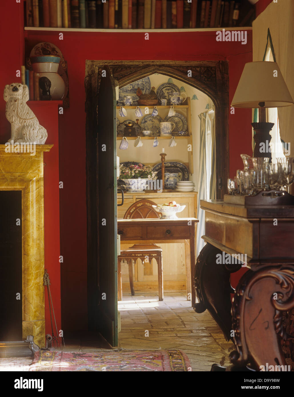 Salle à manger rouge avec porte voûtée de style gothique avec vue jusqu'à la table en pin et chaise dans chalet cuisine Banque D'Images