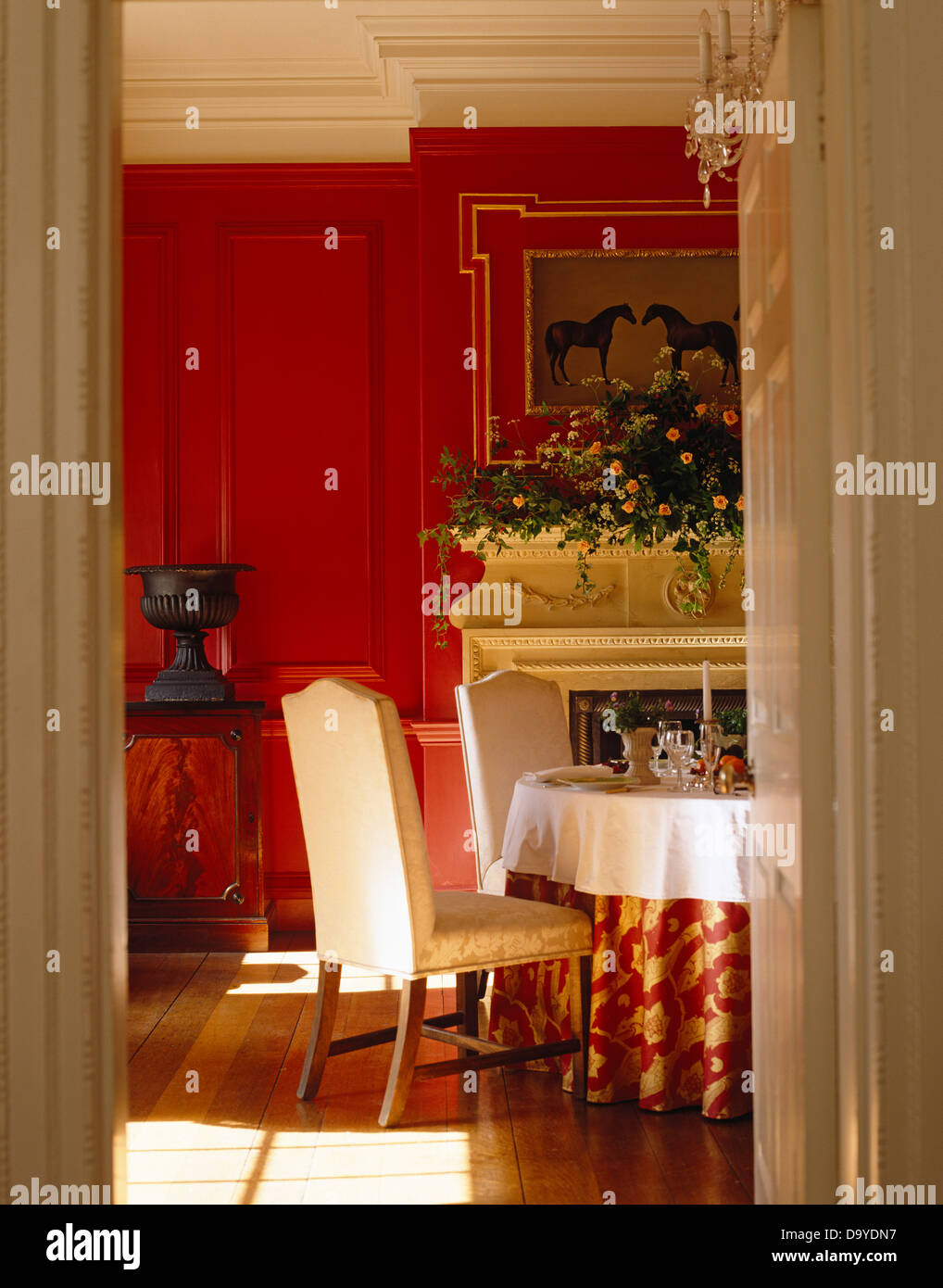 Salle à manger aux boiseries rouge avec fauteuils rembourrés à table avec un tissu à motifs rouge en face de cheminée avec guirlande de fleurs Banque D'Images