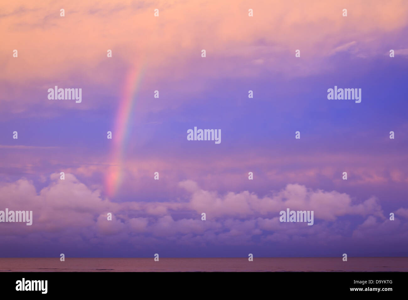 Un arc-en-ciel lumineux arches sur une mer rose dans un vieux rose et violet magenta ciel, encadrée par des nuages de magenta Banque D'Images