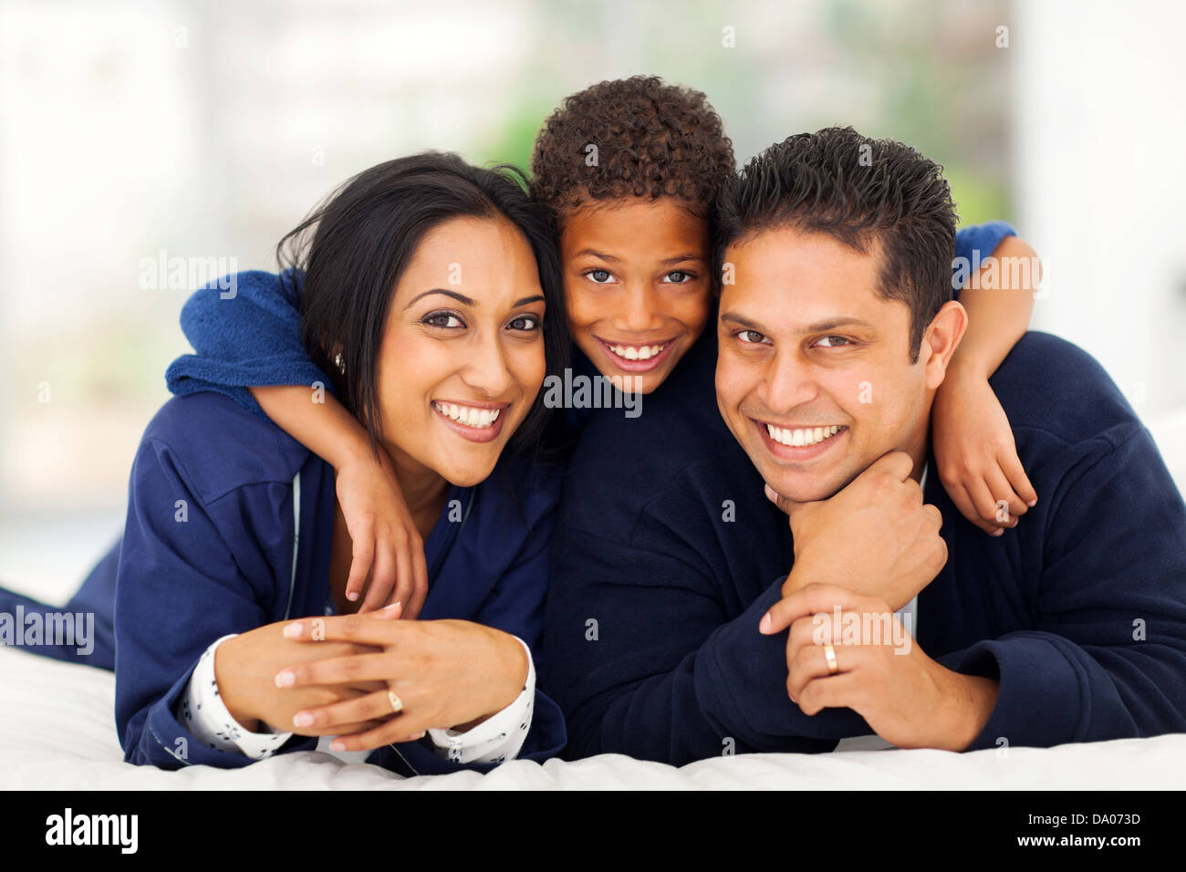 Little Indian boy hugging tandis que ses parents lying on bed Banque D'Images