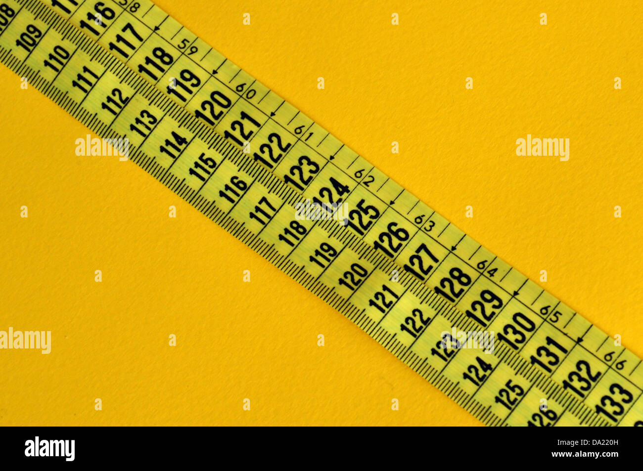 Ruban en plastique mesure pouces et centimètres. Nombres abstraits fond jaune. Banque D'Images
