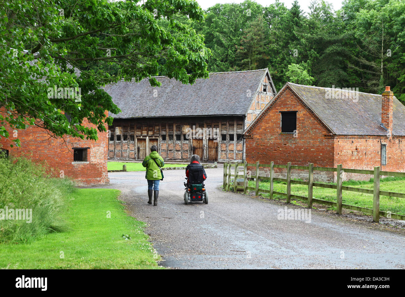 Deux personnes l'un dans un fauteuil roulant en passant devant la grange aux dîmes du 17ème siècle dans le parc du Hodnett Hall Shropshire England UK Banque D'Images