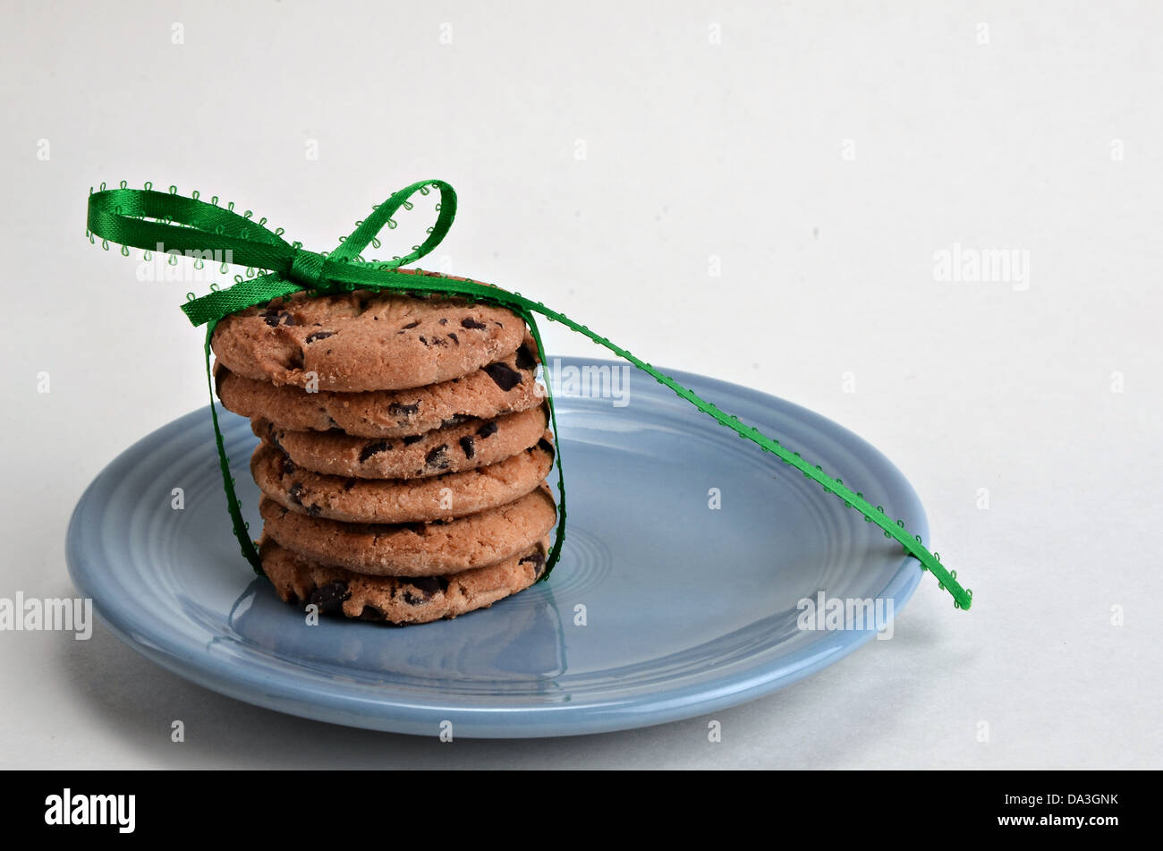 Une pile de cookies aux pépites de chocolat avec un ruban vert et l'arc sur un fond blanc. Banque D'Images