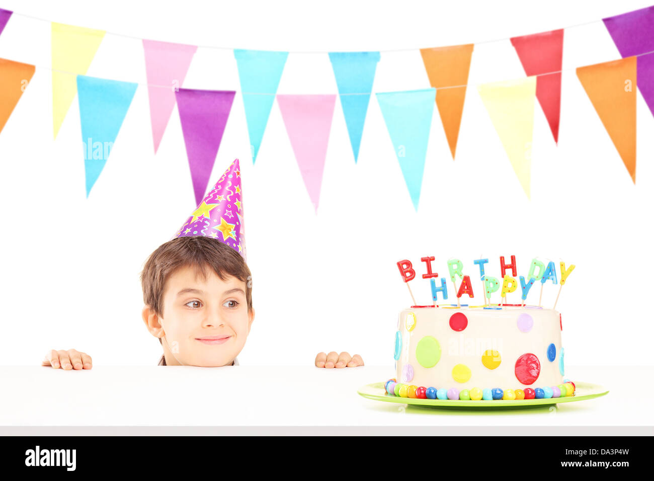 Smiling boy with party hat looking at a birthday cake isolé sur fond blanc Banque D'Images