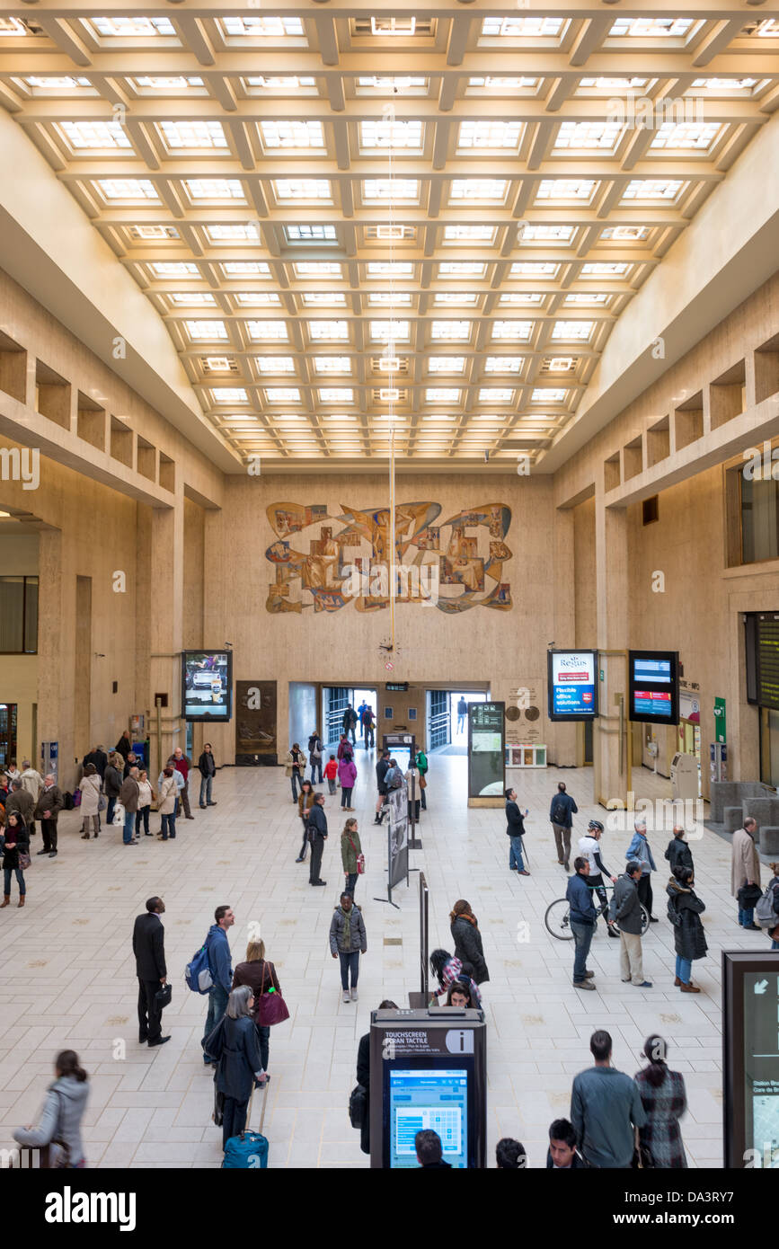 Bruxelles-Central Station Concourse Bruxelles Belgique | BRUXELLES, Belgique — les voyageurs traversent le hall principal de Bruxelles-Central Station sous un plafond à caissons et une grande murale, faisant partie d’un terminal conçu par Victor Horta et achevé après sa mort par Maxime Brunfaut. La gare a ouvert ses portes en 1952 et se classe aujourd'hui parmi les hubs ferroviaires les plus fréquentés de Belgique, reliant les villes haute et basse de la ville sous terre. Banque D'Images