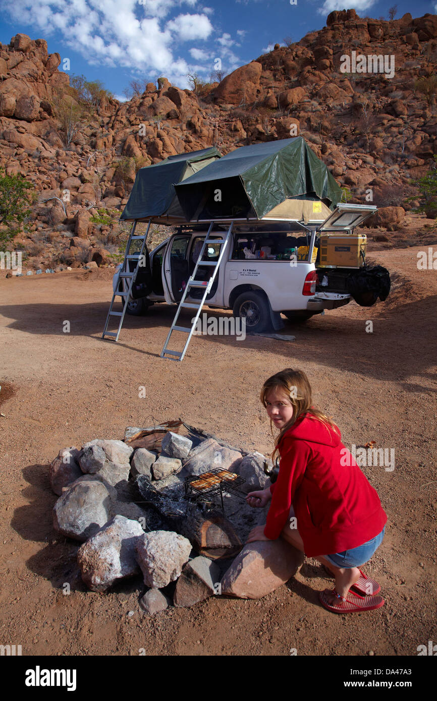 Fille toast de cuisson sur un feu de camp au camping au Mowani Mountain Camp, près de Twyfelfontein, Damaraland, Namibie, Afrique Banque D'Images