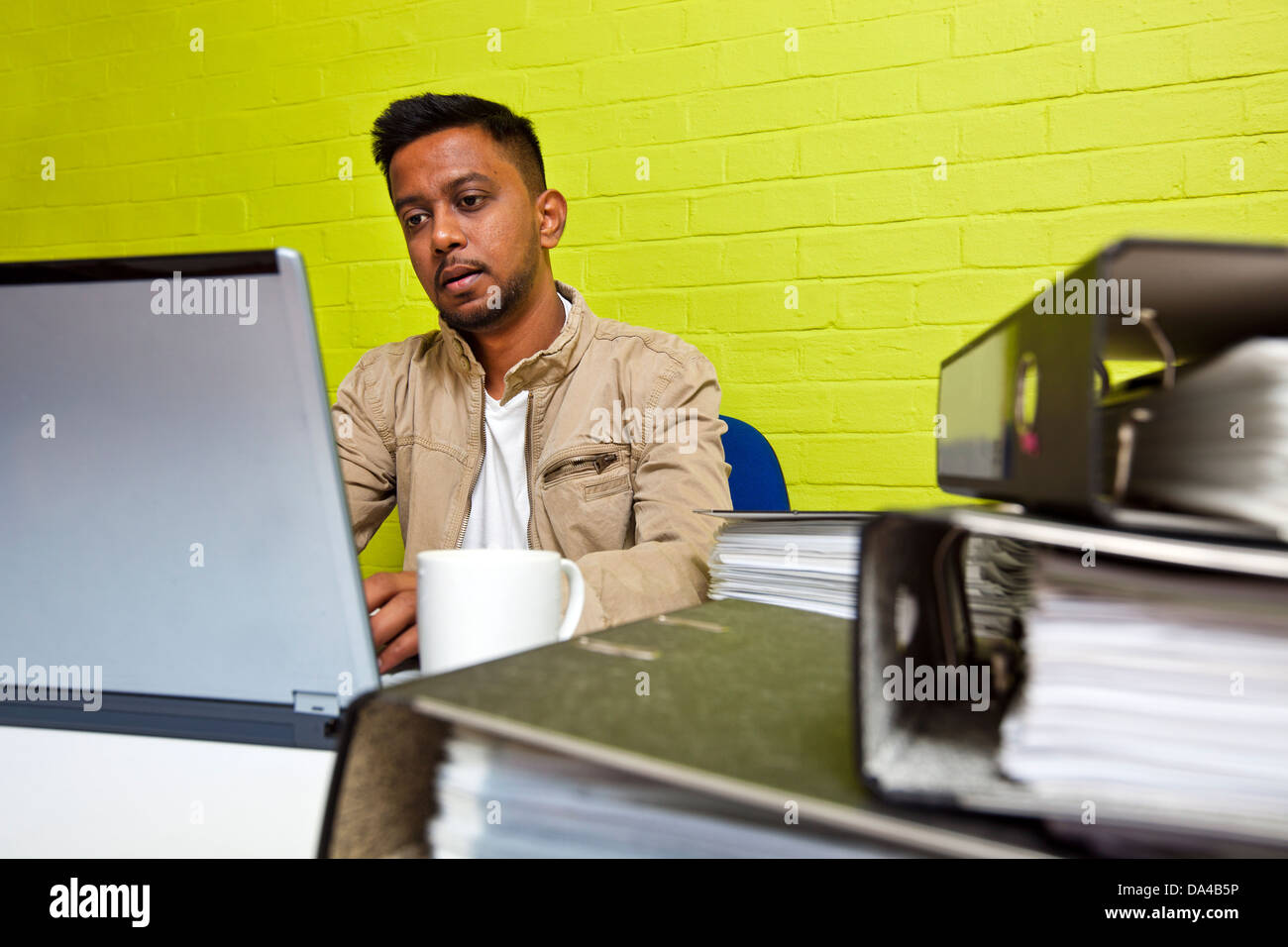 Jeune Indien homme travaillant à son ordinateur entouré par dossiers Banque D'Images