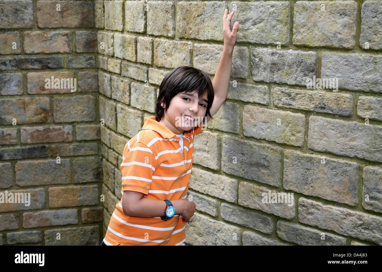 Portrait of smiling brunette boy leaning on stone wall with arms raised Banque D'Images