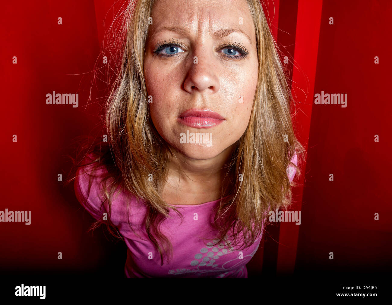 Un curieux woman peering at camera with attitude dans un stand rouge Banque D'Images