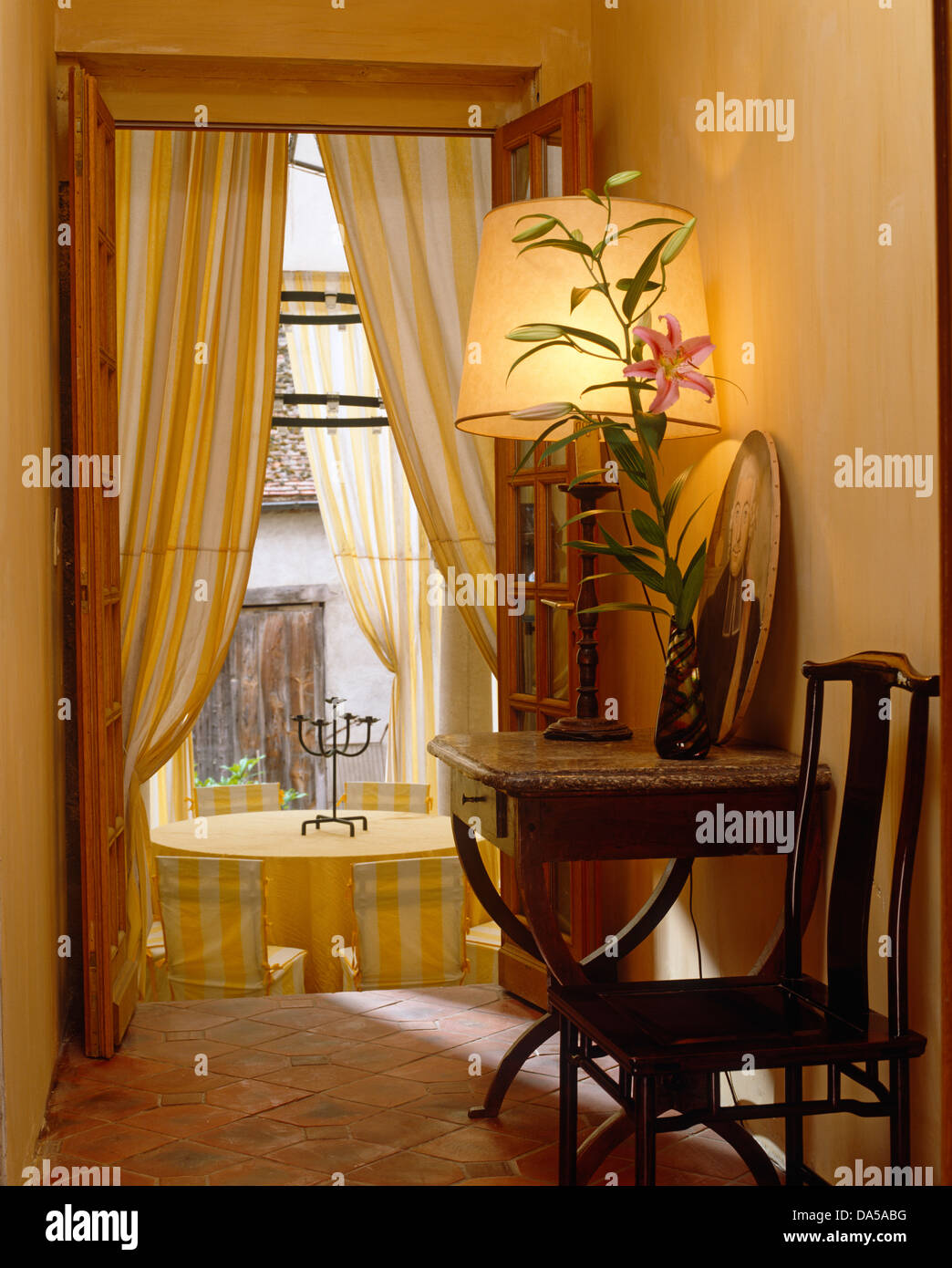 Chaise et table en bois ancien avec la lampe allumée en français salle avec rideaux à rayures jaunes sur porte de salle à manger Banque D'Images