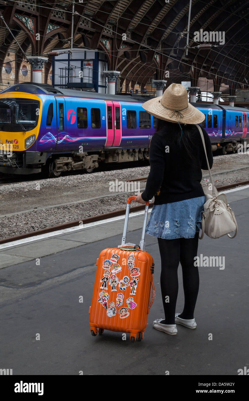 Touriste étranger en attente de banlieue, avec une assurance portant des autocollants, valise pour le transport ferroviaire à la gare de New York, Yorkshire, UK Banque D'Images