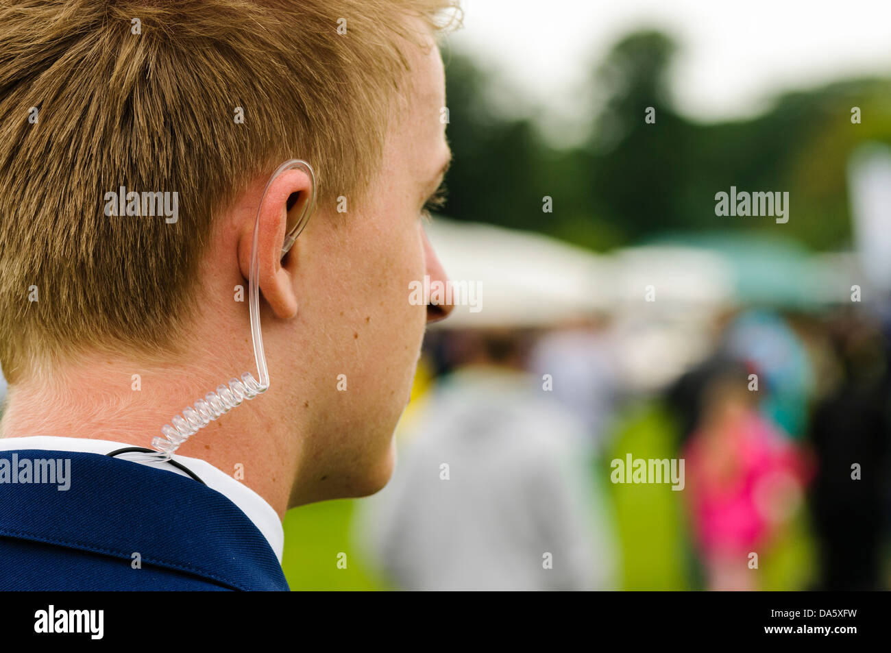 Un jeune gardien de sécurité portant un écouteur enroulé d'écouter sa radio bidirectionnelle Banque D'Images