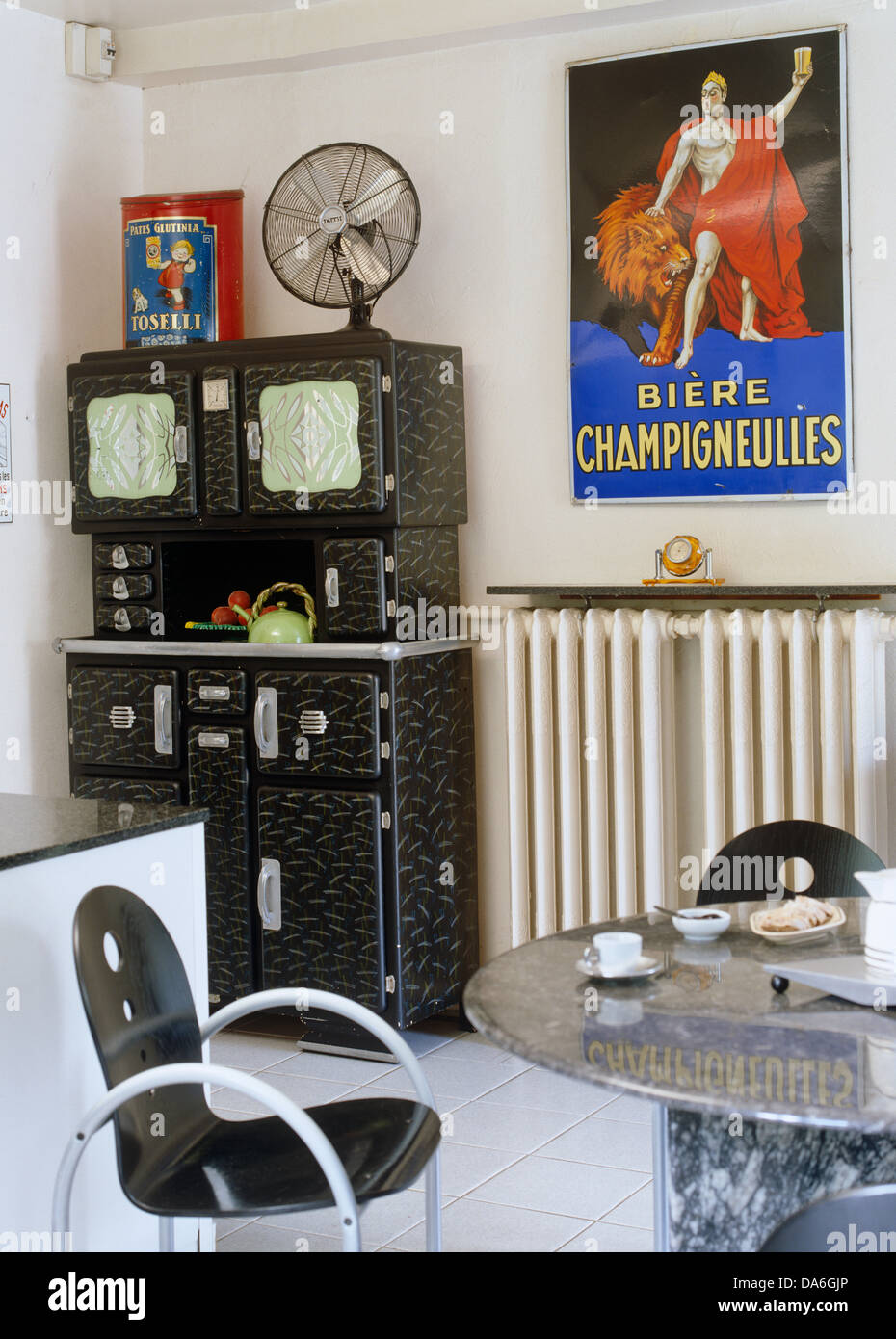 Commode années 50 noir et des chaises à la table de marbre circulaire dans la salle à manger de style rétro avec affiche colorée au-dessus de radiateur Banque D'Images