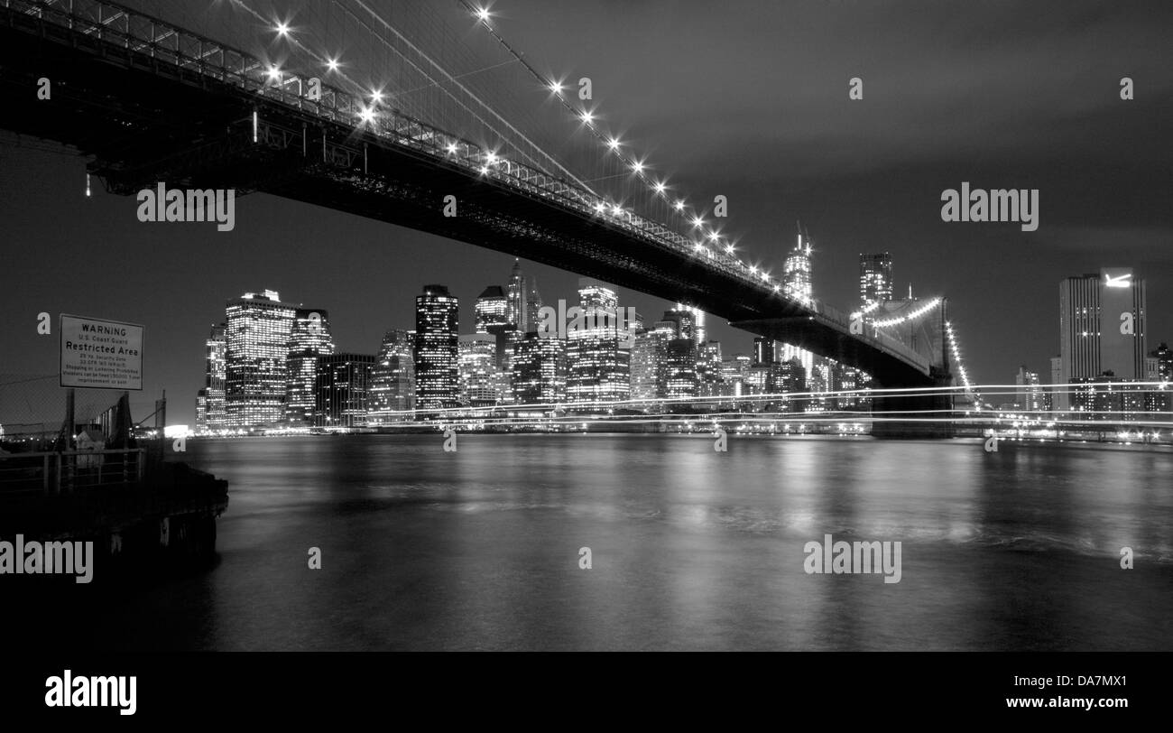 Pont de Brooklyn et le centre-ville de Manhattan au crépuscule, avec des sentiers de lumière à partir d'un bateau qui passe Banque D'Images
