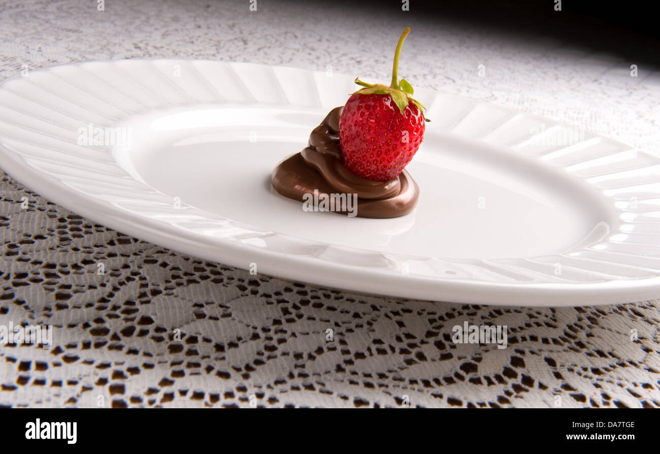 Strawberry assis dans tourbillon de chocolat sur plaque blanche Banque D'Images