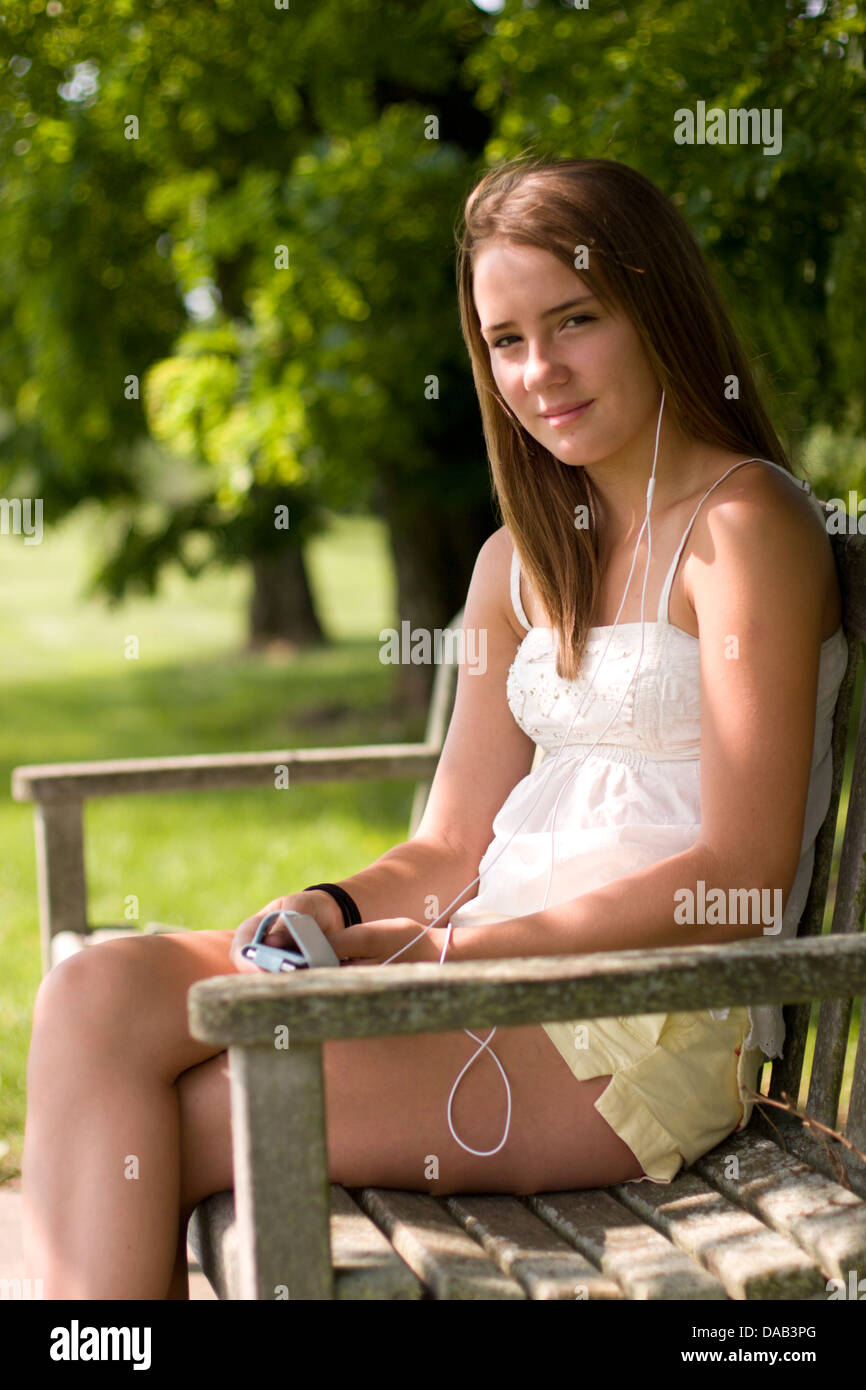 Une jeune fille à l'écoute de la musique sur un banc de parc Banque D'Images