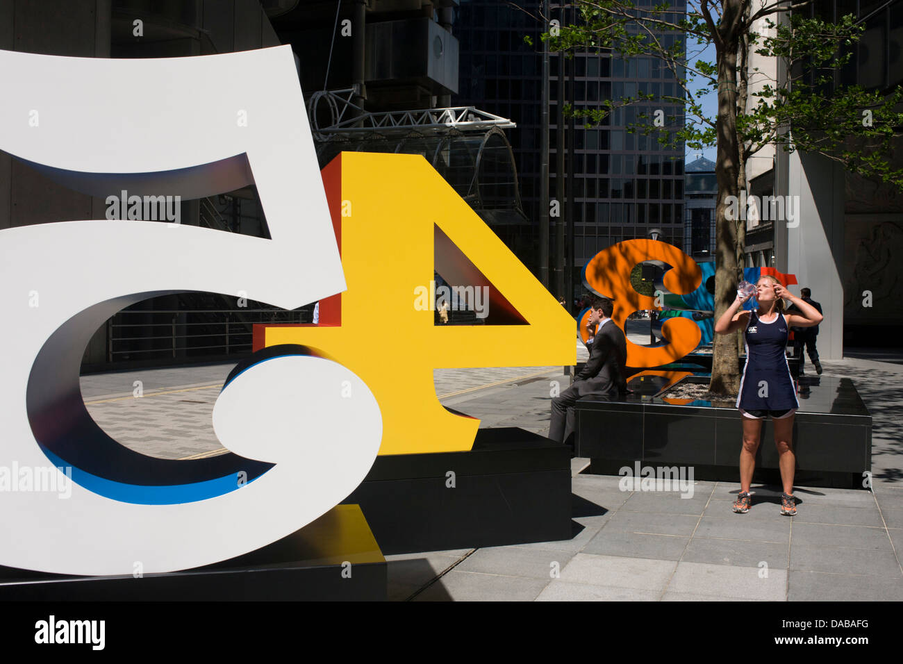 Un travailleur de la ville fume une cigarette comme une femme boit de l'eau à côté d'une installation artistique intitulée "Un à zéro (les dix chiffres)" par l'artiste pop américain Robert Indiana (b 1928), dans la région de Lime Street, City de Londres, la capitale le Square Mile, et son coeur financier. Situé dans le Square Mile, son coeur financier, sont des bureaux environnants et le siège social de la finance et de l'assurance, notamment d'être à proximité du bâtiment de la Lloyds de Londres. Banque D'Images