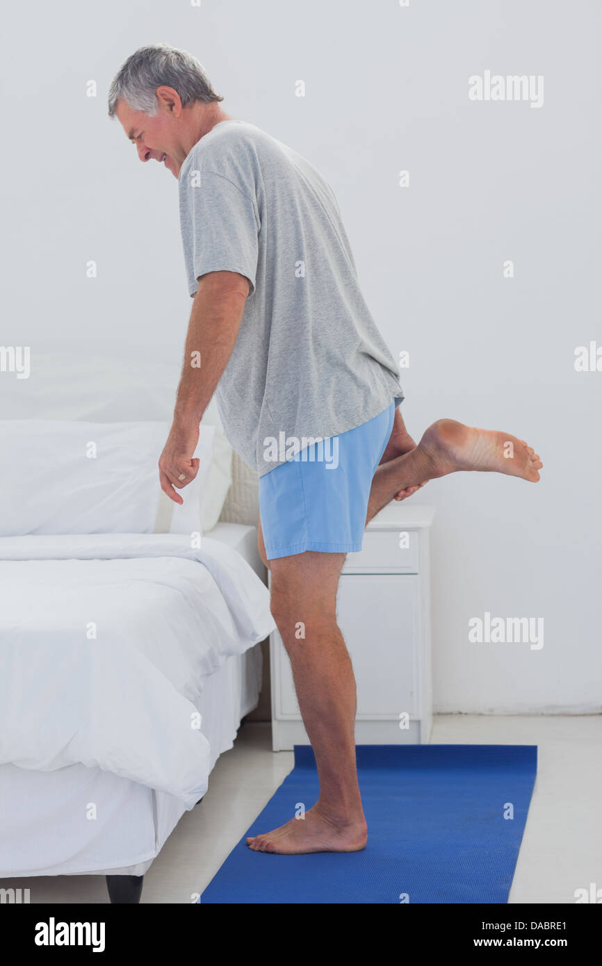 Homme mature étend sa jambe sur un tapis aérobie Banque D'Images
