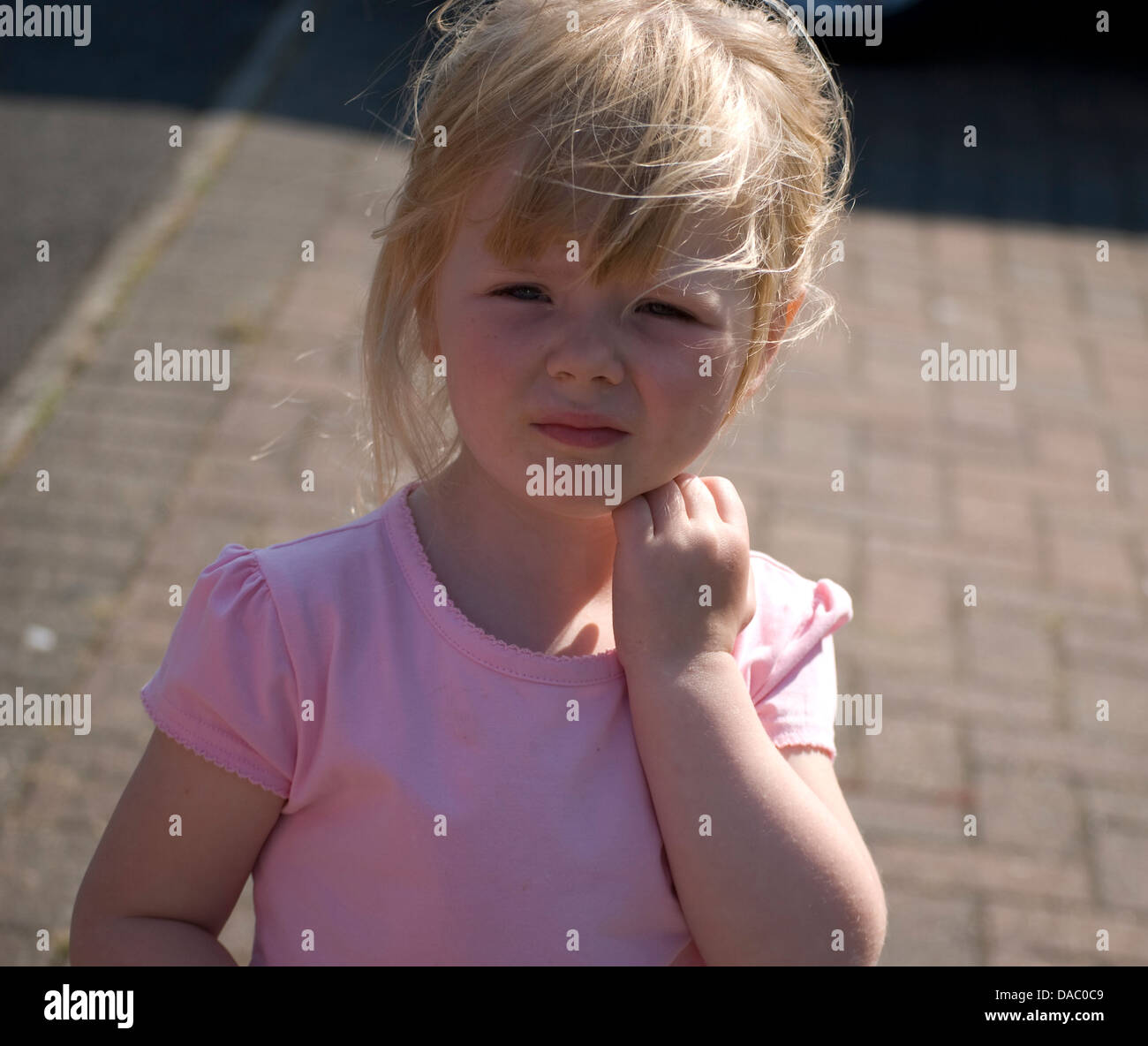 Cute Girl cute little girl debout sur le chemin avec un haut rose et elle est scrathing sur son visage avec sa main gauche. Banque D'Images