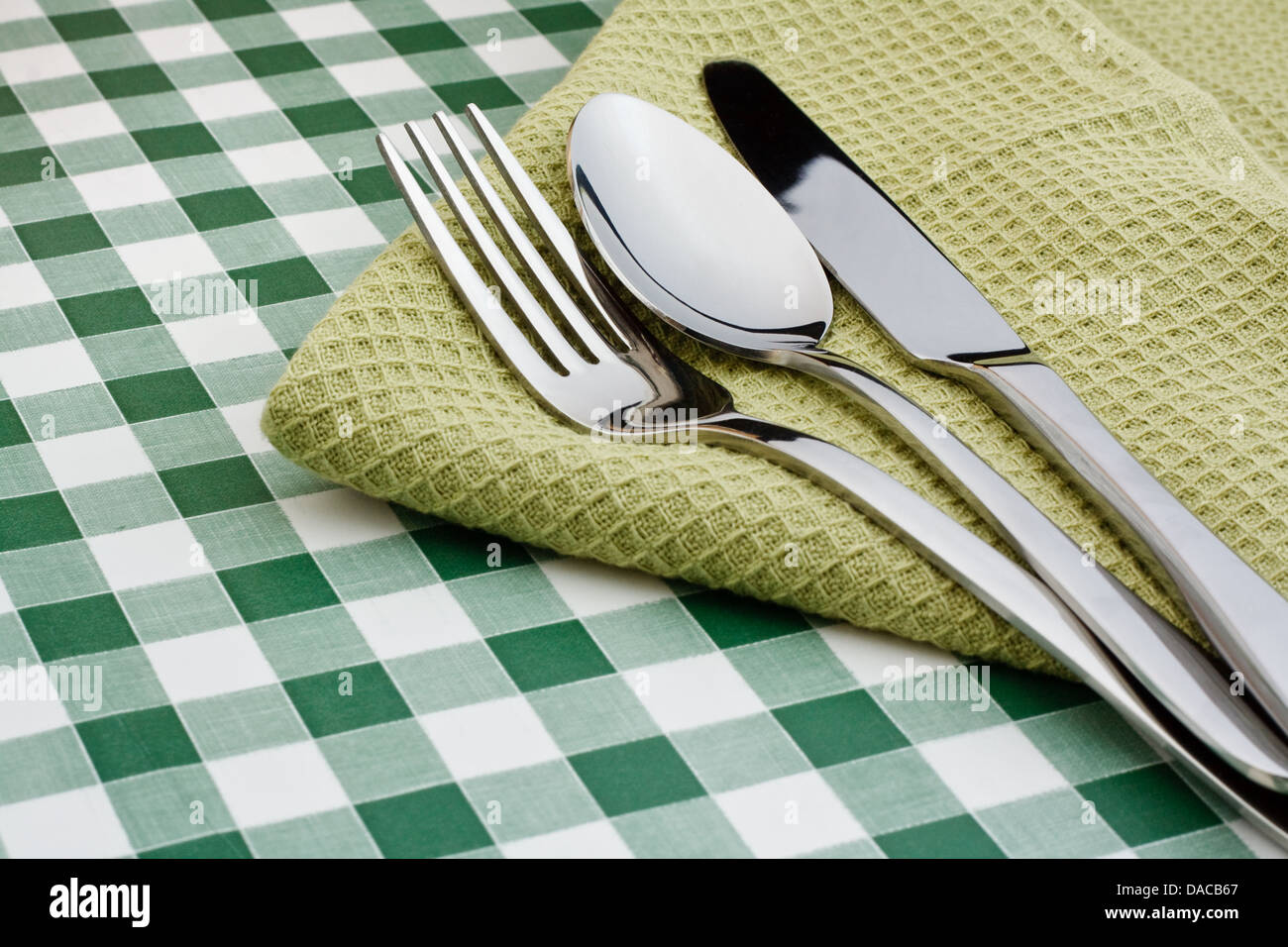 Couteau, fourchette et cuillère sur une serviette verte avec un fond vichy symbole populaire pour restaurants Banque D'Images Couteau, fourchette et cuillère sur une serviette verte avec un fond vichy symbole populaire pour restaurants Banque D'Images