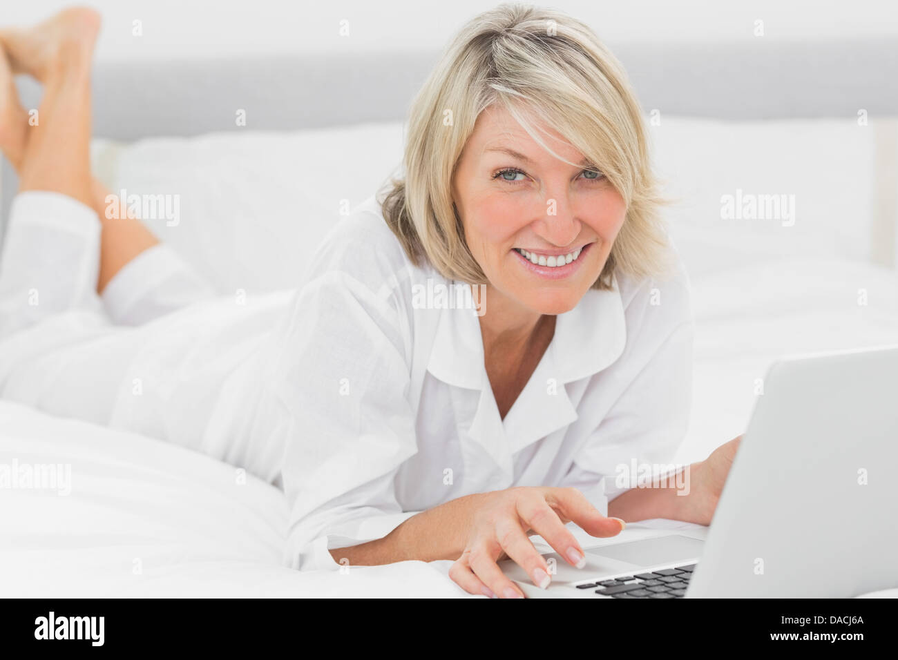 Femme heureuse en utilisant son ordinateur portable sur son lit smiling at camera Banque D'Images