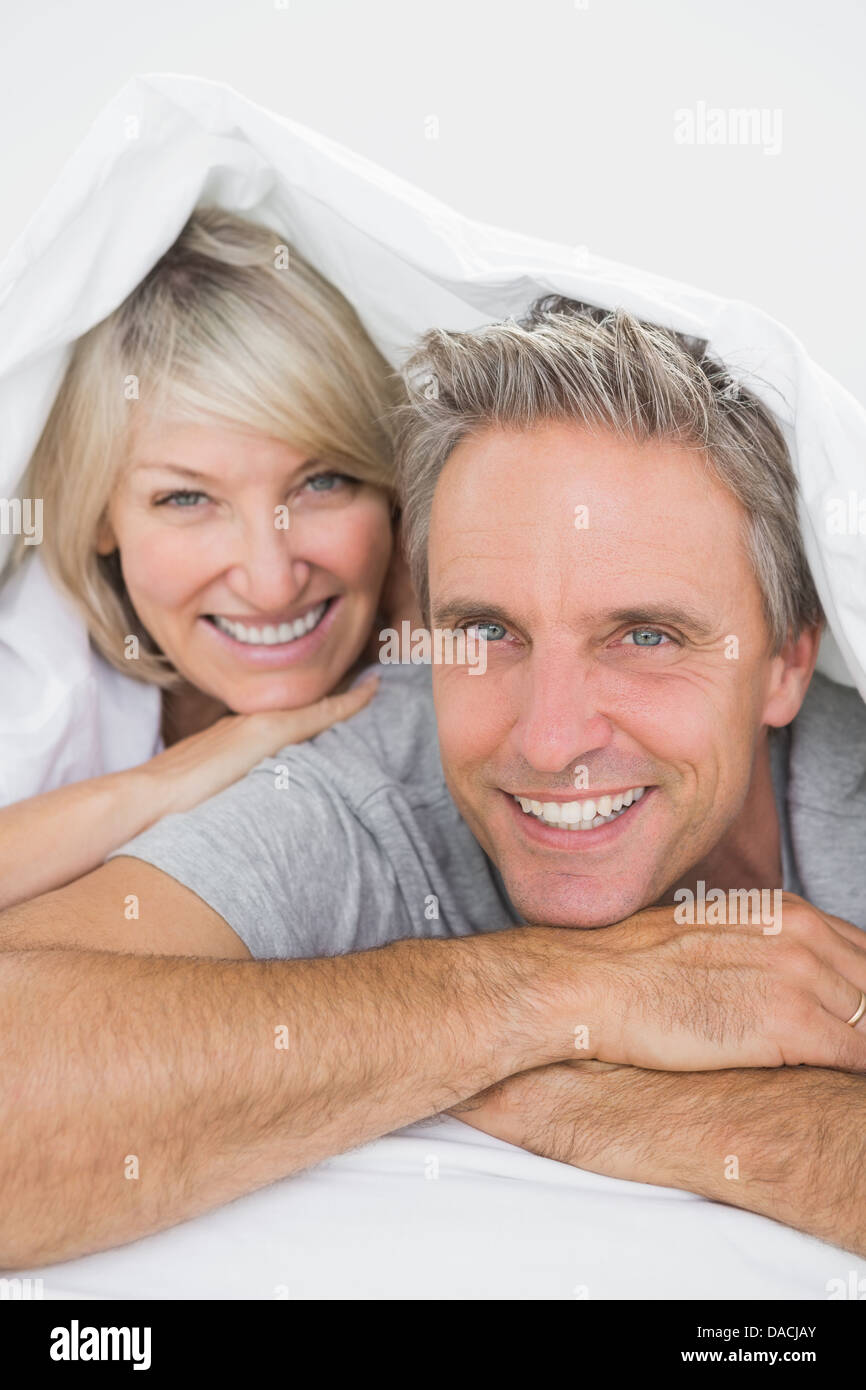 Couple smiling sous les couvertures à l'appareil photo Banque D'Images