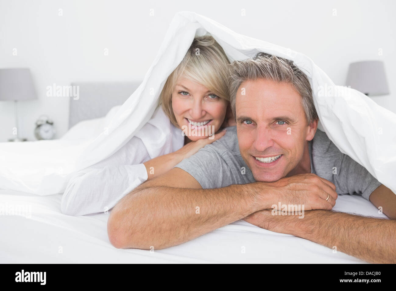 Heureux couple smiling sous les couvertures à l'appareil photo Banque D'Images