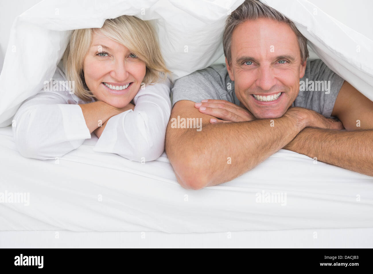 Cheerful couple smiling sous les couvertures à l'appareil photo Banque D'Images