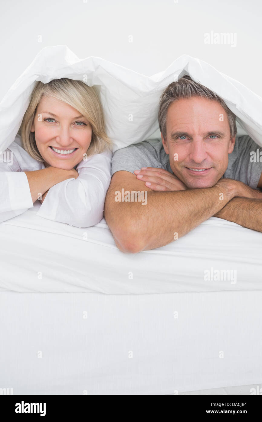 Beau couple smiling sous les couvertures à l'appareil photo Banque D'Images