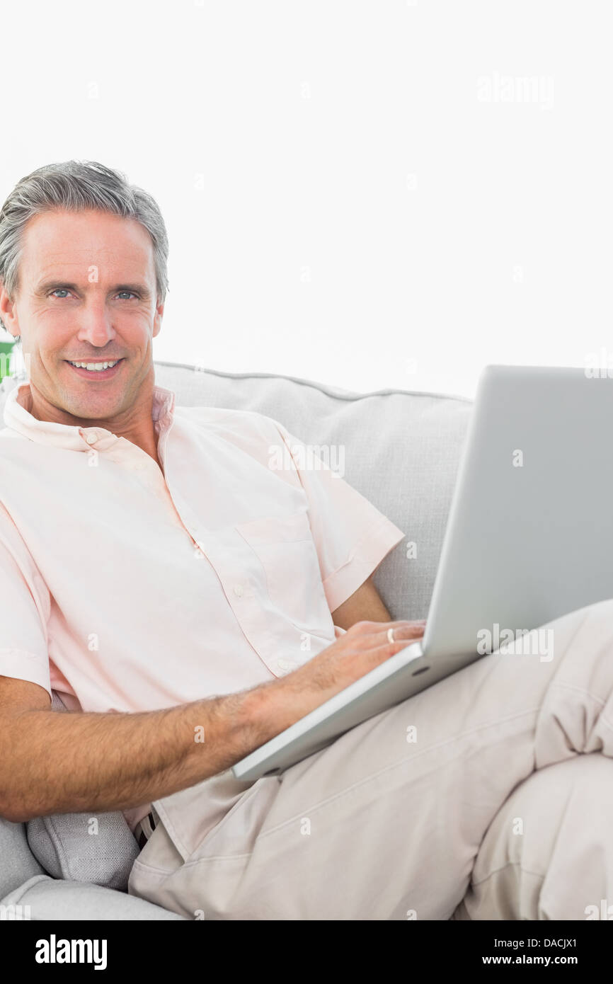 Smiling man sur son canapé en utilisant laptop looking at camera Banque D'Images