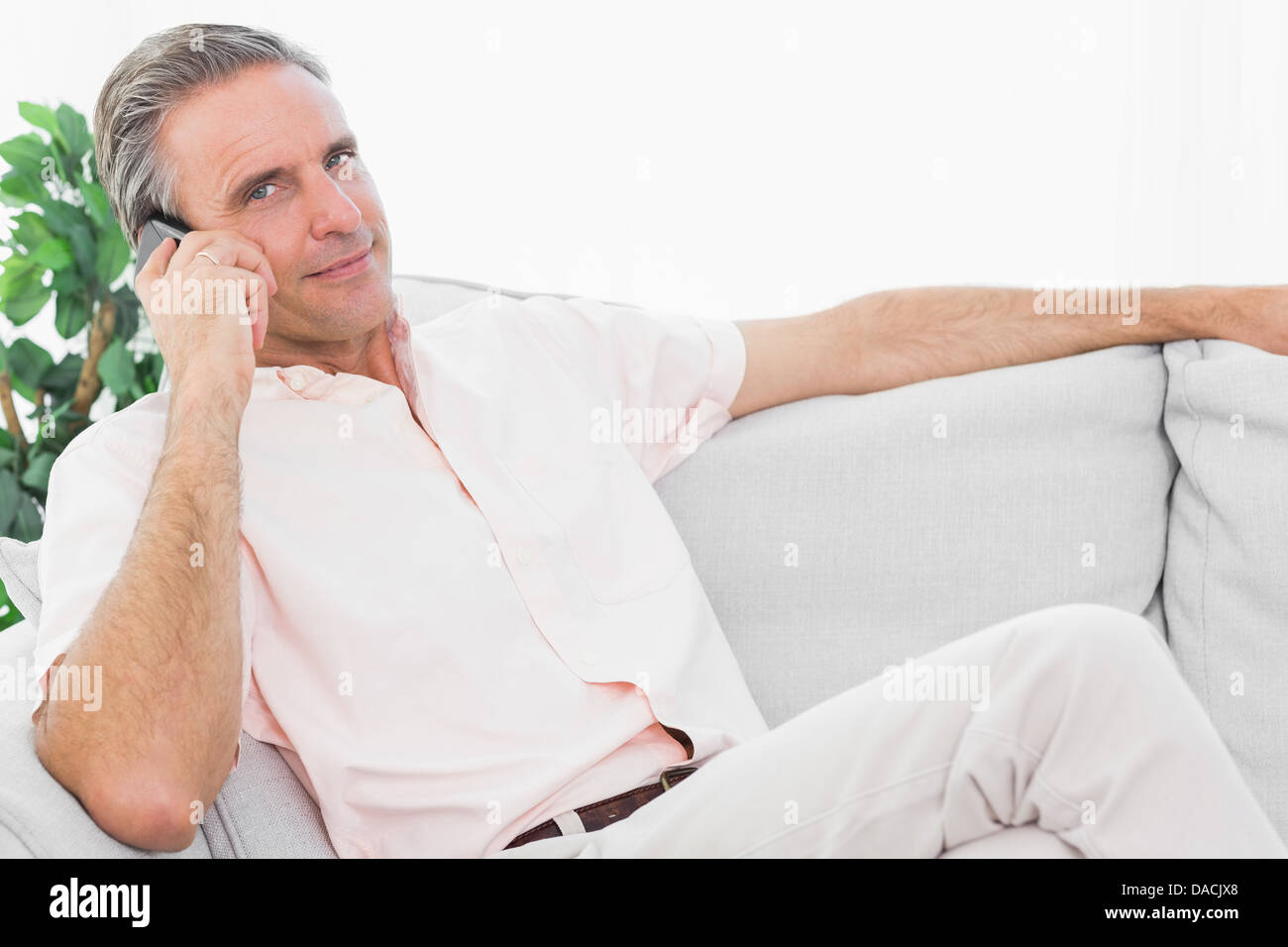 L'homme sur son canapé au téléphone smiling at camera Banque D'Images