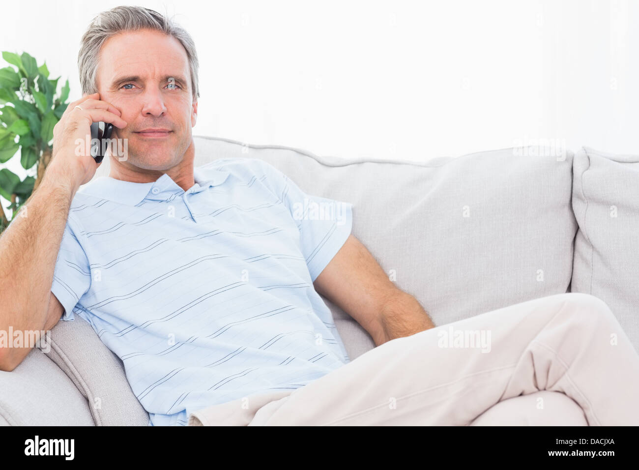L'homme sur son canapé making phone call and smiling at camera Banque D'Images