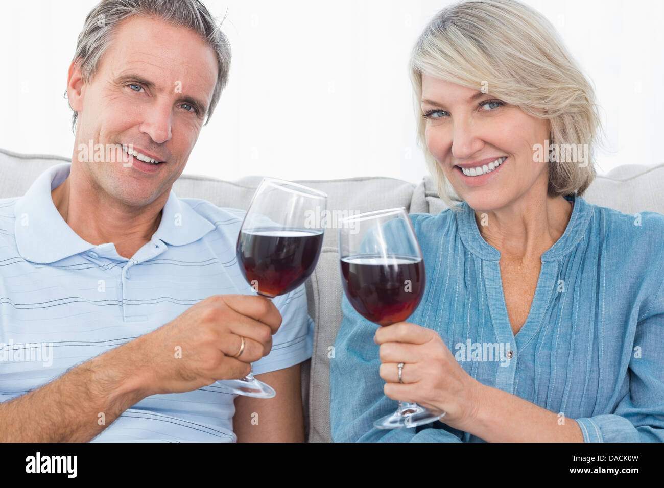 Couple toasting with red wine sur le canapé smiling at camera Banque D'Images